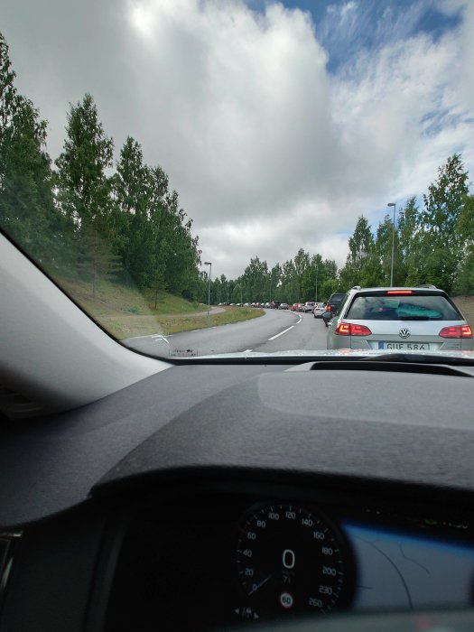 Körfält i trafik med olika bilar sett från förarsätet med sikt framåt och bilens instrumentbräda synlig.
