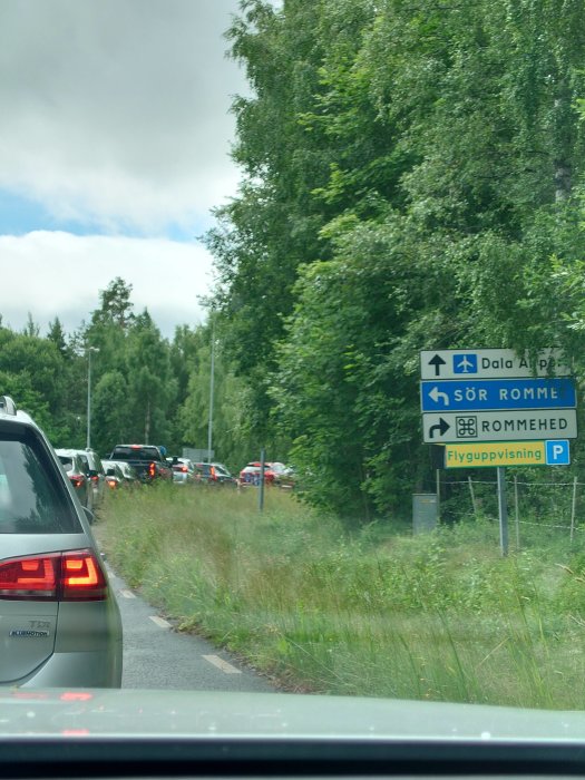 Trafikkö på landsväg med skylt mot Dala Alperna och Romme, tagen från bilens förarsida.