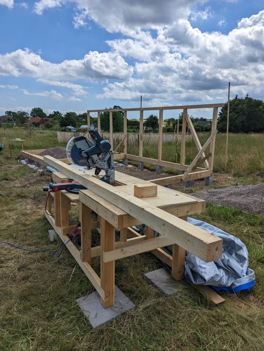 Grundläggande träarbetsbänk med en monterad klyvsåg, utomhus på en gräsmatta under byggnation.