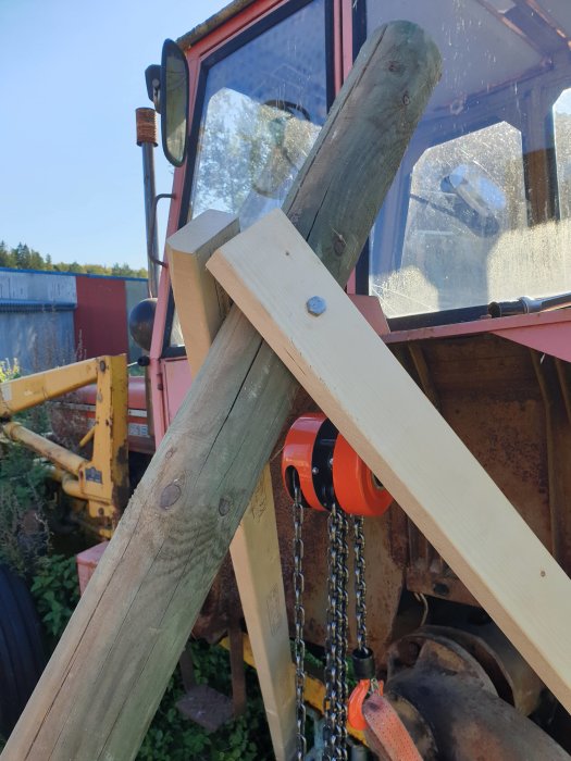 Trästolpe och plankor mekaniskt förstärkta med bultar vid sidan av en traktor.