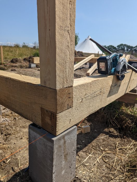 Hörntapp i träkonstruktion med tapphål klart och en cirkelsåg i bakgrunden på byggarbetsplats.