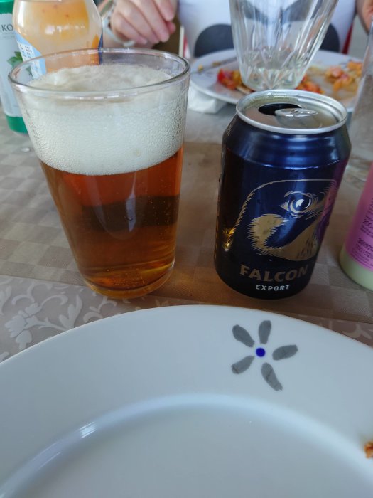 Ett glas med öl bredvid en Falcon Export burk på ett bord med matrester.