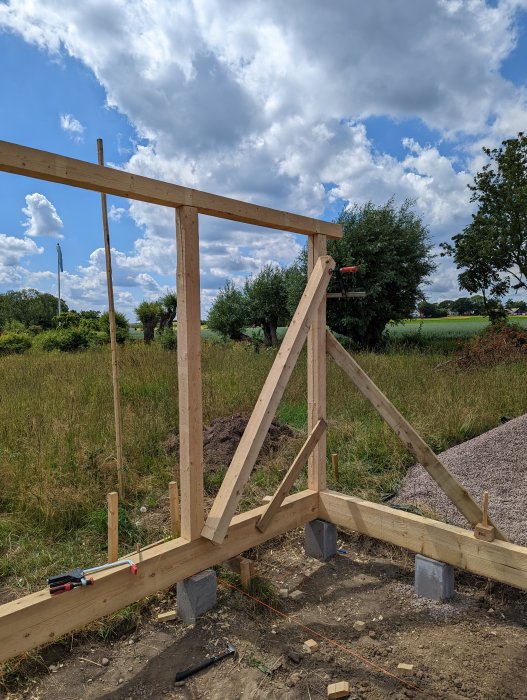 Träramverk för byggprojekt med fixerade snedsträvor och verktyg på marken under en molnig himmel.