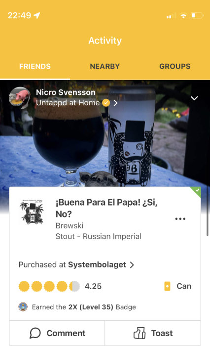 Ett glas mörk öl bredvid en ölburk med konstnärlig etikett på ett utomhusbord.
