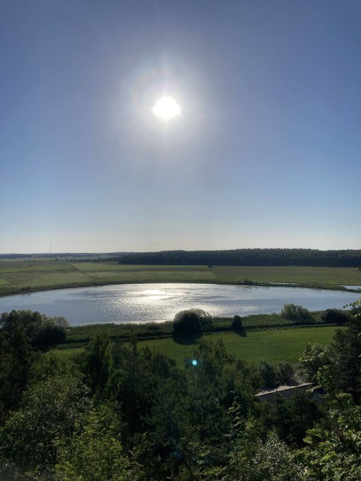 Solnedgång över en lugn sjö med omgivande grönska och reflektioner i vattnet.