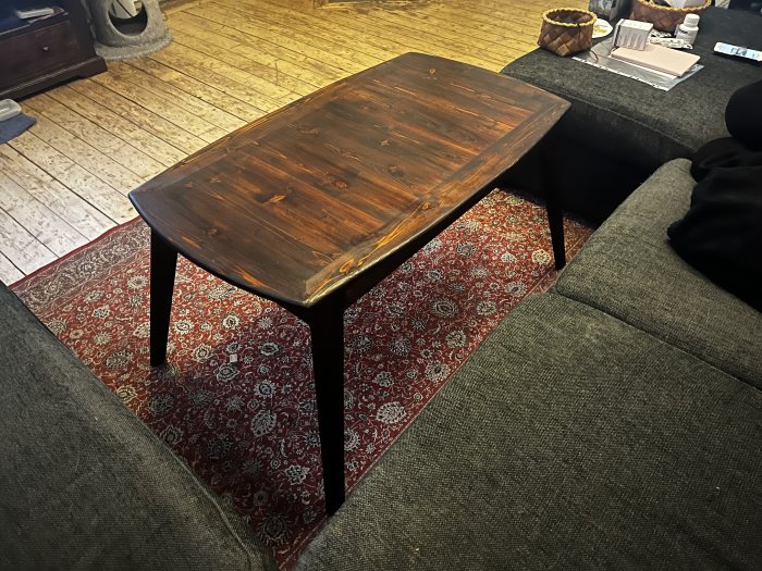 Träsoffbord med mörkbrun finish på ett röd- och beige-mönstrat matt, framför en grå soffa.