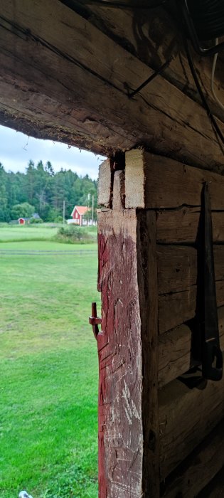 En bearbetad trästock med insatta klossar och vinkeljärn vid en gammal rödmålad byggnads hörn.