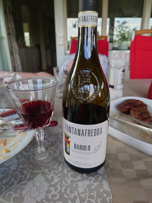 Flaska Fontanafredda Barolo 2017 och ett glas rödvin på bord med matrester.