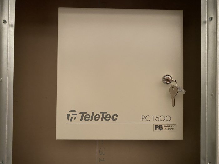 Larmcentral märkt "TeleTec PC1500" med nycklar i låset och säkerhetsdekal.