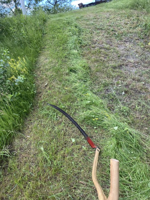 Liegande grässlänt med en handhållen lie, använd för att röja gräs.