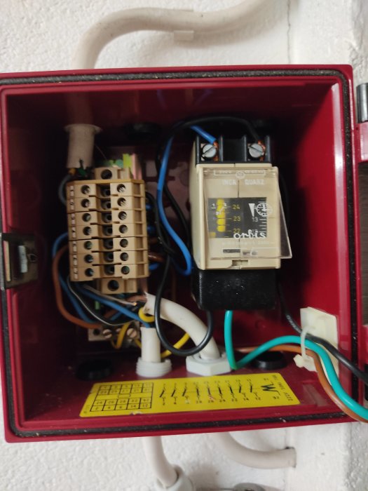 Öppen elektrisk klockstyrning med synliga kablar och anslutningar på en röd monteringsplatta.