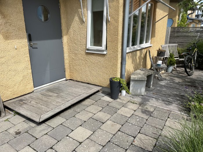 Entrétrappa i ek och angränsande trätrall vid husets entré, bredvid grå stenplattor.