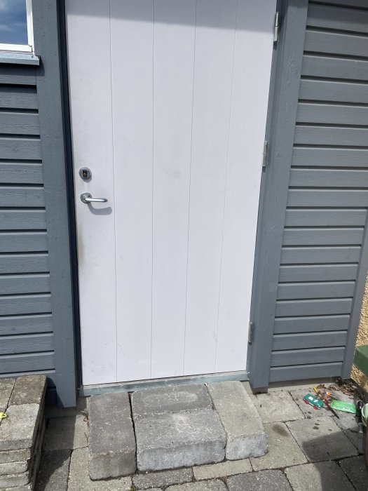 En enkel entrétrappa av släta betongplattor framför en vit dörr och grå vägg.