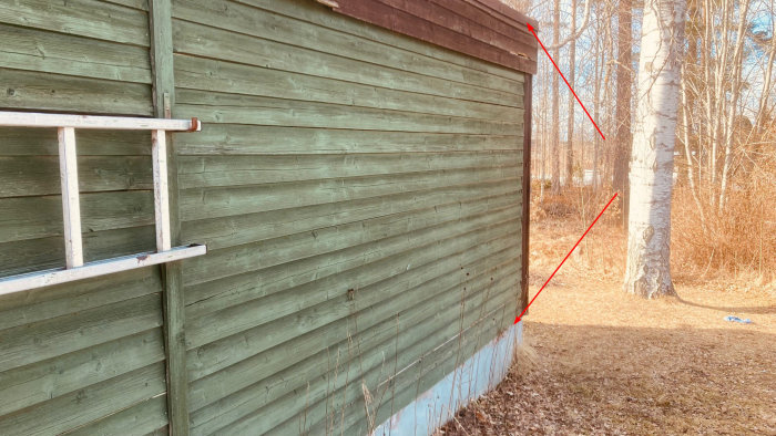 Trött gammal träpanel på ett garage med tydliga tecken på slitage och ingen synlig vindskydd bakom, markerad med röda pilar.