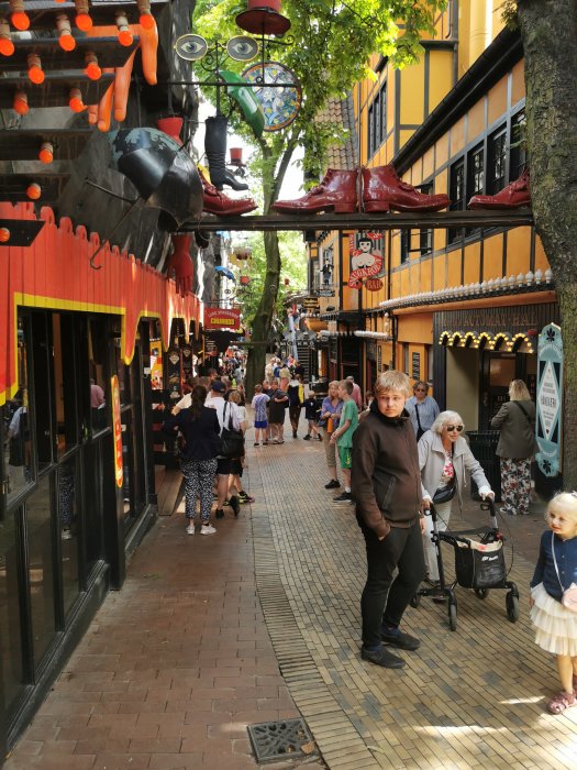 Livlig shoppinggata med unik butiksfasad och dekorationer, besökare går och tittar på butiker.