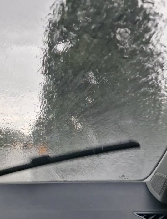 Vy genom en bilruta med tända vindrutetorkare under regnväder.