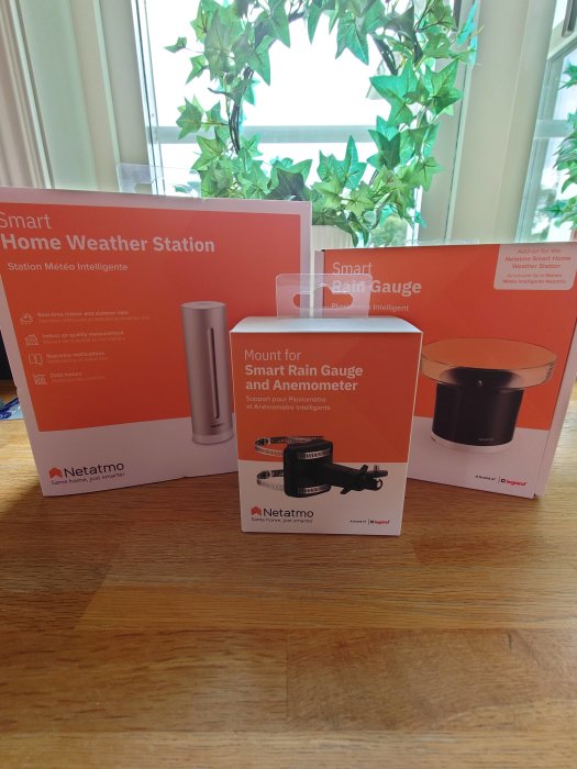 Netatmo Smart Home Weather Station och tillbehör förpackningar på ett bord framför fönster med växter.