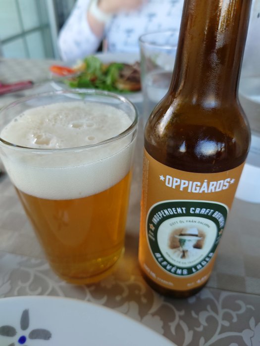Ett glas med ljust öl och en ölflaska från Oppigårds på ett matbord.