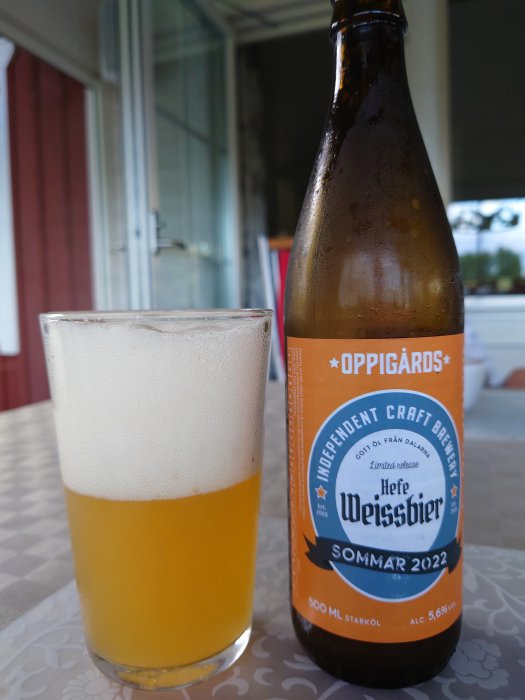 Glas fyllt med veteöl och en flaska Oppigårds Hefe Weissbier på ett bord.