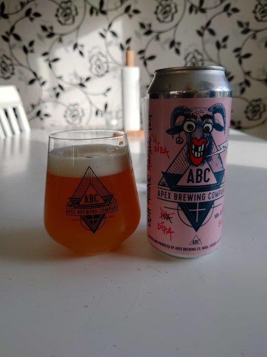 Öppnad burk av Apex Brewing Company öl och ett halvfullt glas mot blommig tapetbakgrund.