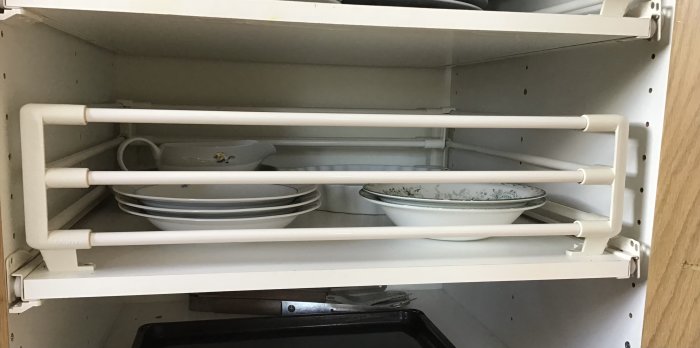 Öppet köksskåp med vitrörshyllor och staplade porslinstallrikar och skålar inuti.