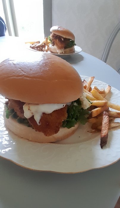 Kycklingburgare med aioli och sallad på bröd, serverad med pommes frites på en tallrik.