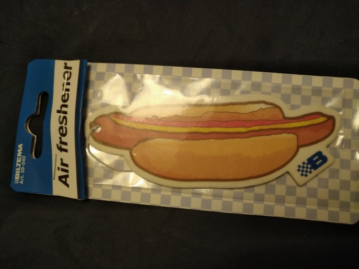 Luftfräschare med hotdog-motiv i förpackning på rutmönstrad bakgrund.