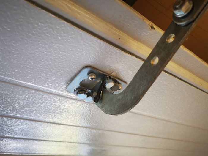 Skadad infästning av portöppnare till garageport med synliga skruvar och delaminerad plåt.