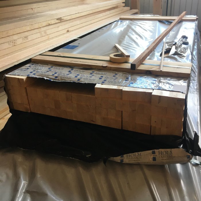 Materialpaket för dörrkarmar ovanpå svart skyddsduk, inklusive träreglar och förpackat virke.