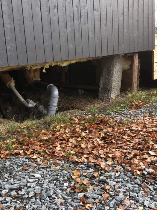 Skadade plintar under en stuga med lutande stöd och isolering som hänger löst, omgiven av höstlöv och grus.