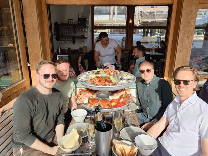 Grupp människor avnjuter skaldjursplatå på restaurang i soligt väder.
