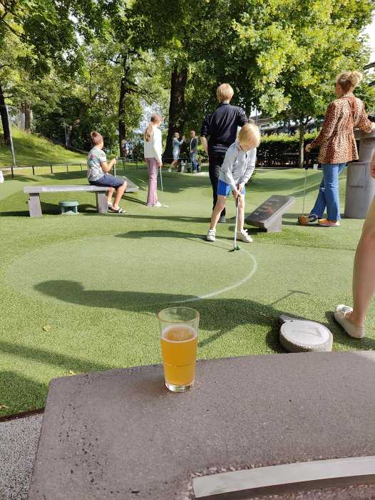 Ölglas på bord framför en minigolfbana med människor som spelar i bakgrunden.