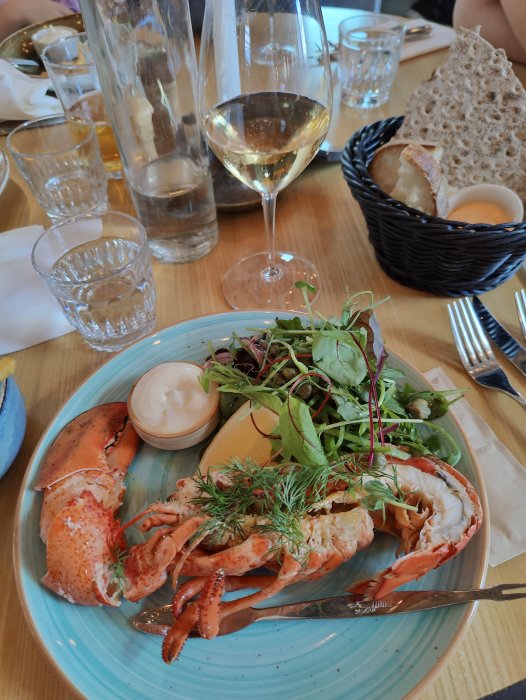 Middag med hummer, sallad, bröd och ett glas vitt vin på en restaurangpier.