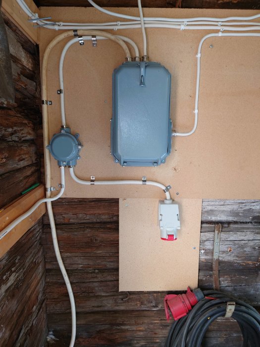 Elektrisk installation i lada med kabelrör, elkabelrulle och strömbrytare på ojämnt trävägg.