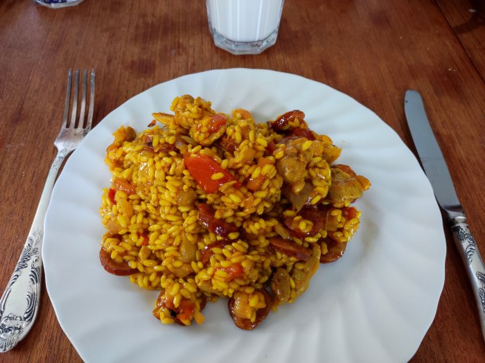 En tallrik med kyckling och ris, kryddat och tillagat i paella-stil, serverat med bestick.