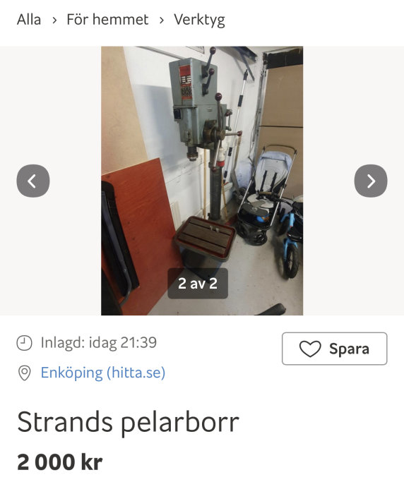 Pillarborrmaskin av märket Strands i ett garage, med verktygslåda och barnvagn i bakgrunden.