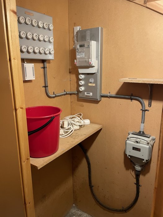 Gammal elcentral i källare med säkringar och en jordfelsbrytare, omgiven av elledningar.