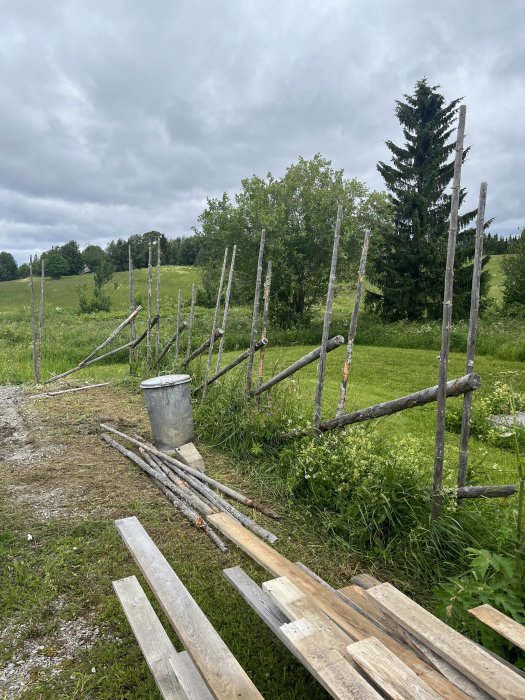 Gammal hundgård nära grönt fält och skog med träslanor och hink i förgrunden.