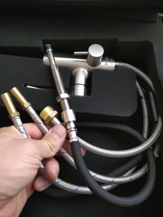 En hand håller en ny Primy Steel Accent köksblandare med sladdar och kopplingar.