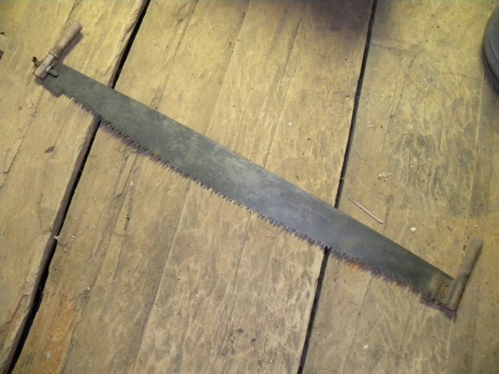 Gammaldags manuell såg med långt tandat blad och trähandtag ligger på ett slitet trägolv.
