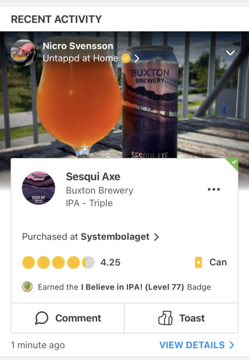 Ett glas med orangefärgad dryck bredvid en burk Buxton Brewery öl på ett räcke utomhus.