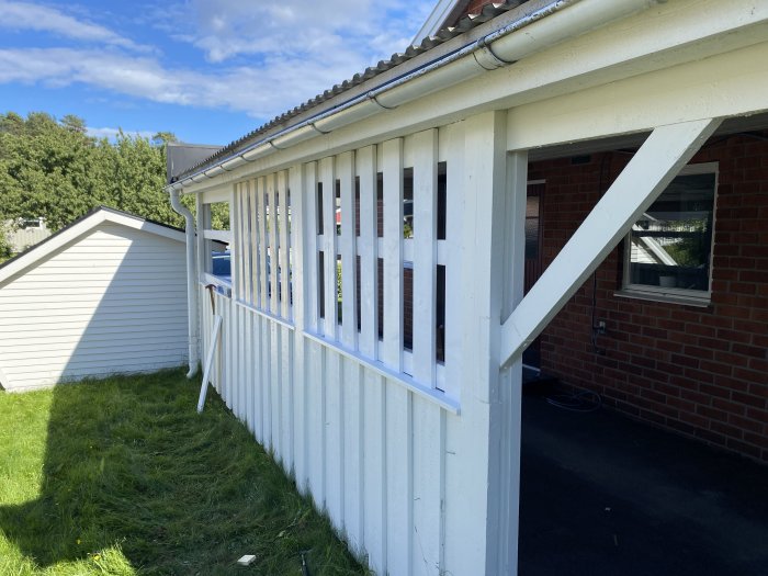 Pågående bygge av träspaljé i vit stolpekonstruktion som ersätter presenning i carport.