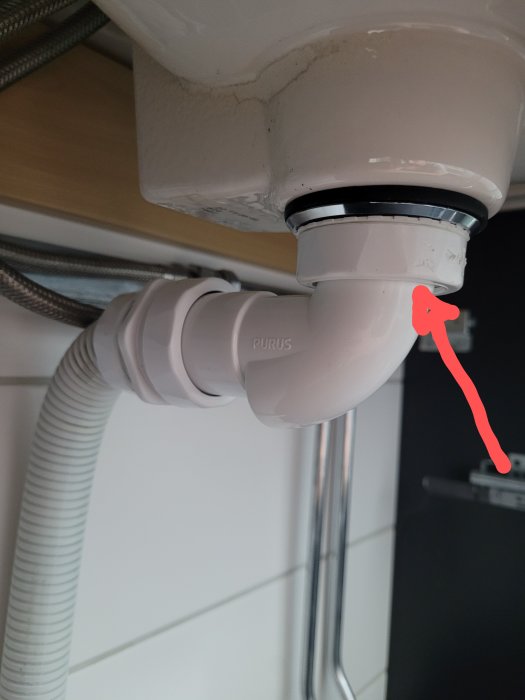 Vattenläcka vid handfatets avloppsanslutning markeras med röd pil.