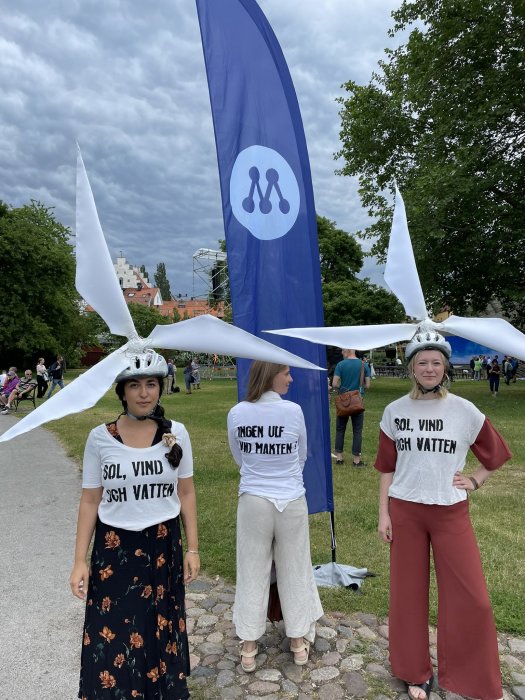 Tre personer med propellerhattar och tröjor som främjar sol, vind och vatten energi.