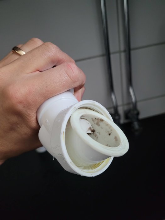 Hand håller ett demonterat rördel i plast som saknar packning med synlig kant och smuts.