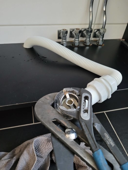 Rördelar och polygrip på bänk, med vattenläckage och rördel som saknar packning.