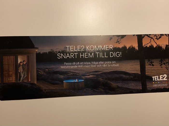 Reklamblad från Tele2 med texten "SNART KOMMER TELE2 HEM TILL DIG!" och bild på en person som tittar ut genom en dörr mot en badtunna vid sjö.