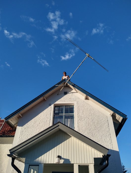 Person som tar ner en gammal TV-antenn från taket på ett hus mot en klarblå himmel.