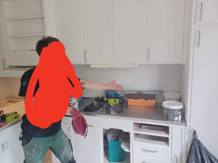 Person pekar på en rostfri diskbänk i ett kök under renovering.