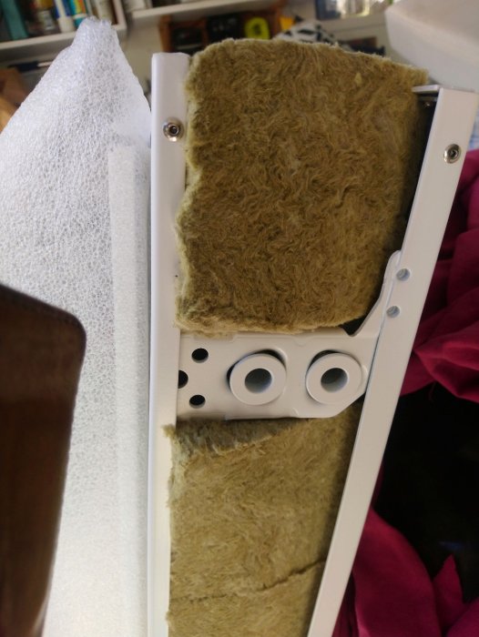 Närbild på hörnet av en vit plåtdörr med monteringshål, inlindad i skyddande bubbelfolie och isolering.